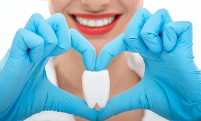 Close portrait of young woman dentist with healthy wide smile holding artificial tooth on white background